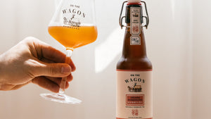 A bottle of On The Wagon Assam & Darjeeling kombucha with a hand holding a glass filled with the beverage. 