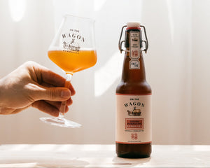 A bottle of On The Wagon Assam & Darjeeling kombucha with a hand holding a glass filled with the beverage. 