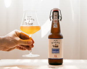 A bottle of Earl Grey On The Wagon kombucha with a hand holding a glass filled with kombucha