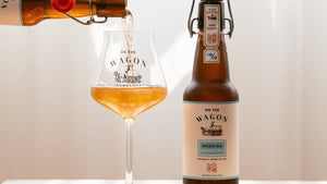 A bottle of On The Wagon Hojicha kombucha being poured into a glass, next to a full bottle of kombucha