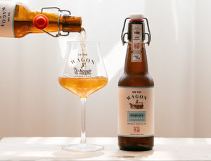 A bottle of On The Wagon Hojicha kombucha being poured into a glass, next to a full bottle of kombucha