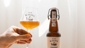 A bottle of On The Wagon Hojicha Kombucha with a hand holding a glass filled with kombucha
