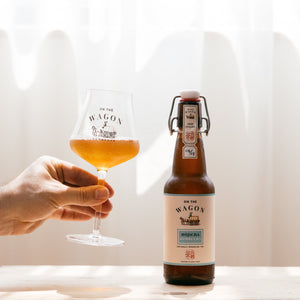 A bottle of On The Wagon Hojicha Kombucha with a hand holding a glass filled with kombucha