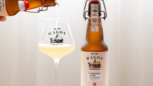 Pouring golden kombucha into a sleek glass with a cold, swing-top bottle next to it. Lemongrass & Lime.