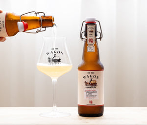Pouring golden kombucha into a sleek glass with a cold, swing-top bottle next to it. Lemongrass & Lime.