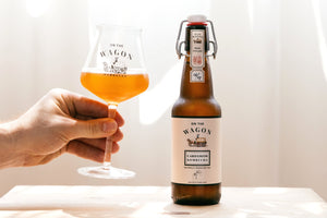 On The Wagon Cardamom & White Tea Kombucha bottle and hand holding a glass filled with kombucha