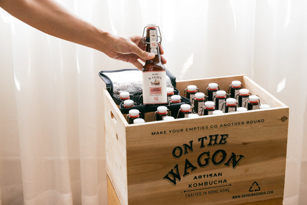 A box full of On The Wagon Kombucha with a hand taking out 1 bottle