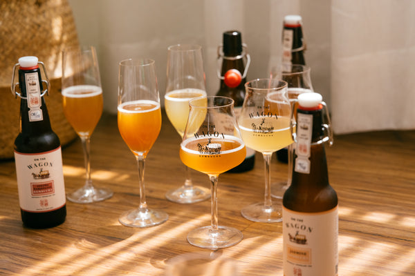4 few bottles of On The Wagon Kombucha in different flavors, and 5 glasses filled with different kombucha liquid