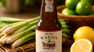 Bottle of 'On the Wagon' Lemongrass & Lime flavored kombucha with lemons, limes, and lemongrass on a wooden surface