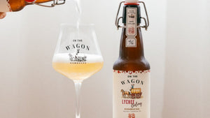 Bottle of 'On the Wagon Lychee' Kombucha being poured into a glass with a white background.