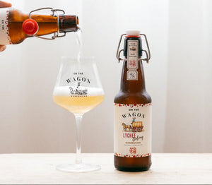 Bottle of 'On the Wagon Lychee' Kombucha being poured into a glass with a white background.